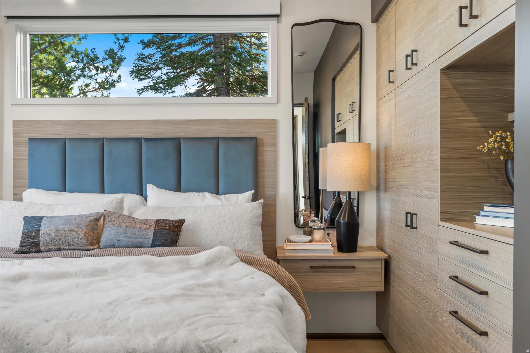 Built-in wood-finish cabinetry, integrated floating nightstand, transom window, full-length mirror with a curved frame, and a panel-tufted headboard