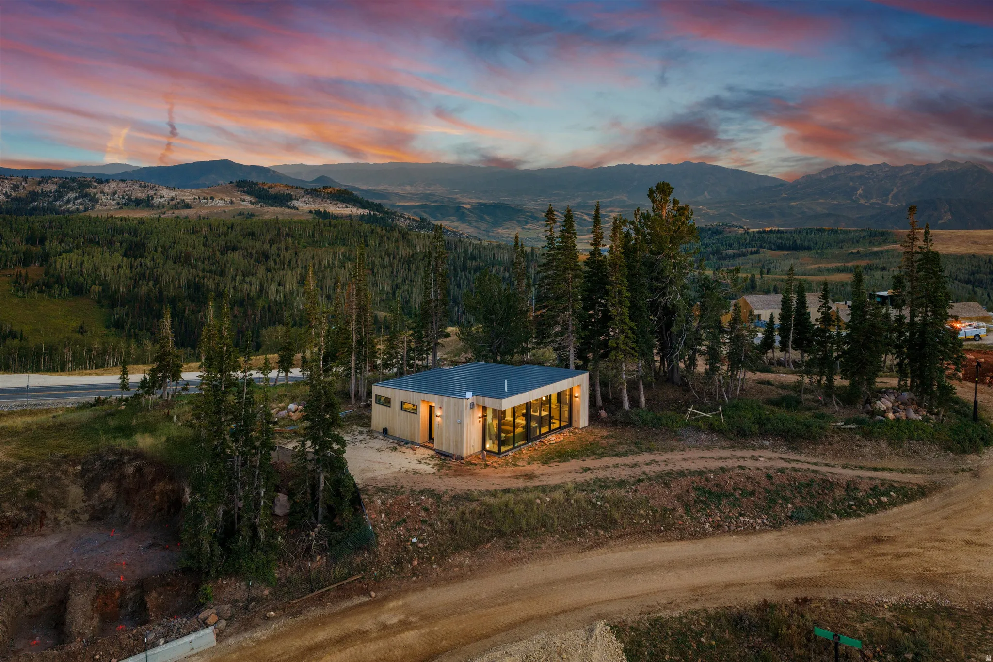 Modern residential structure nestled among mature evergreen trees on expansive grounds, featuring illuminated exterior walls, clean geometric lines, and panoramic mountain and valley vistas across the surrounding landscape