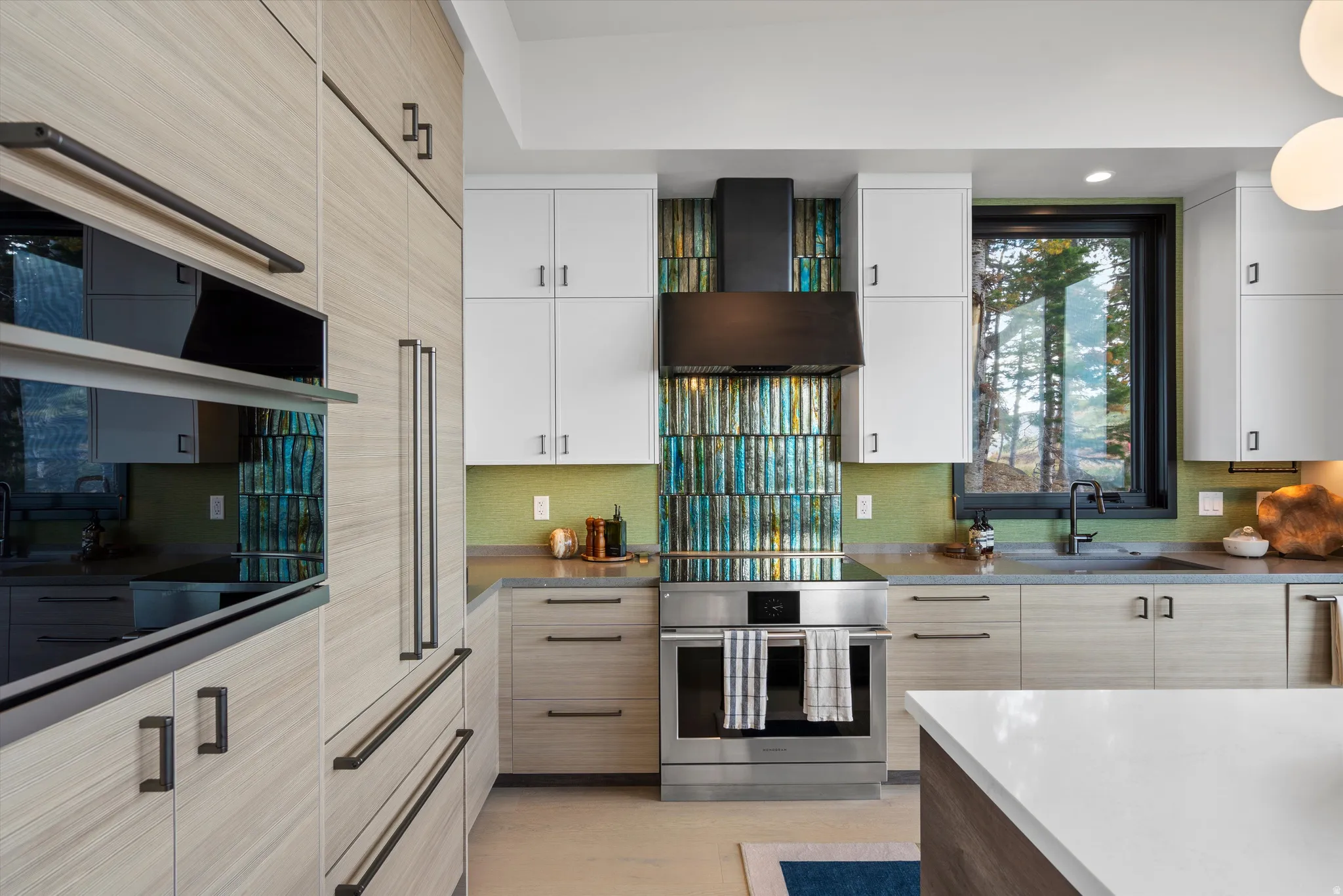 Modern kitchen featuring integrated appliances, light wood-finish cabinetry, a striking multi-tone backsplash, and light countertops