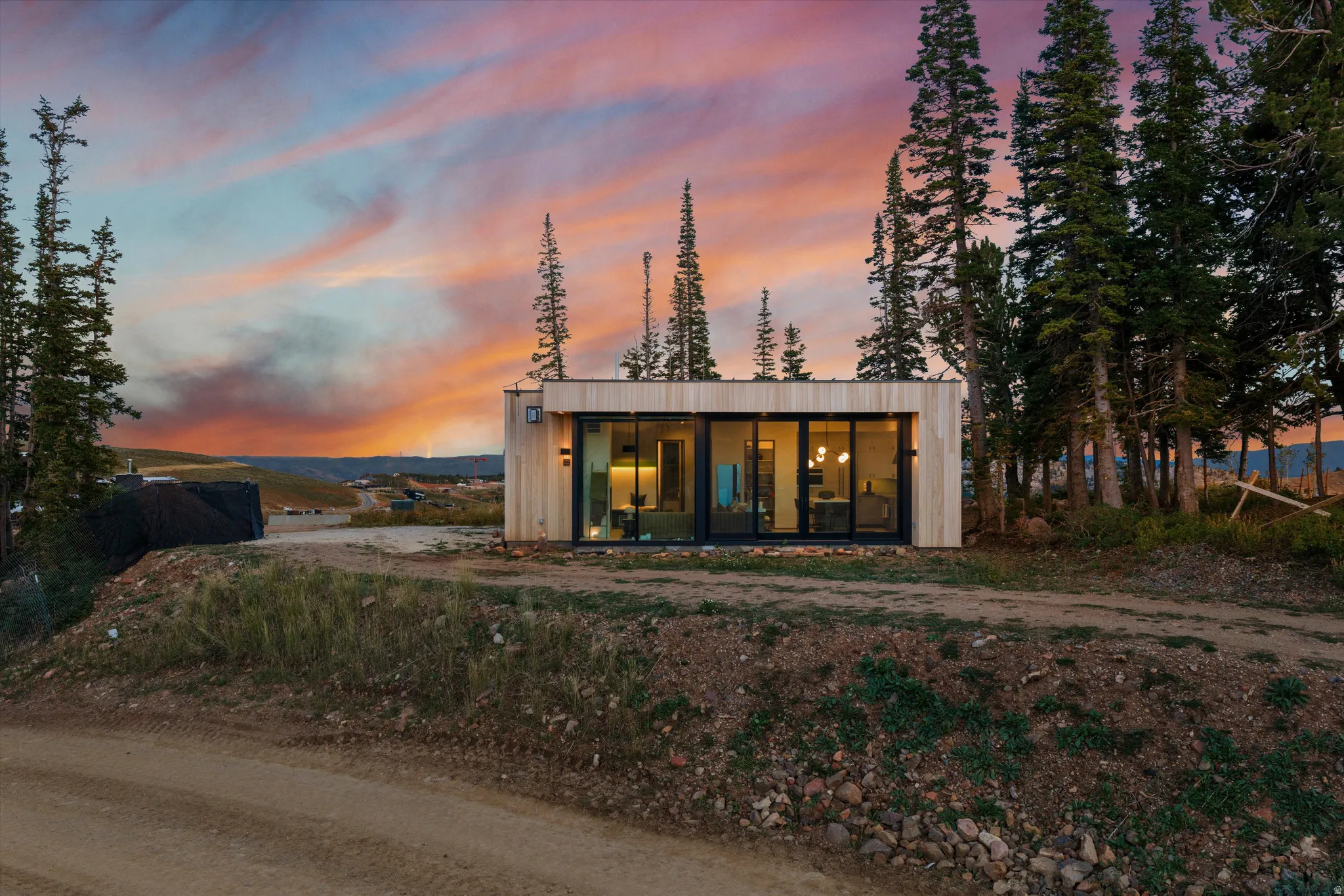 Modern single-story residence featuring light wood-panel siding, large glass sliding doors, and surrounding mature evergreen trees