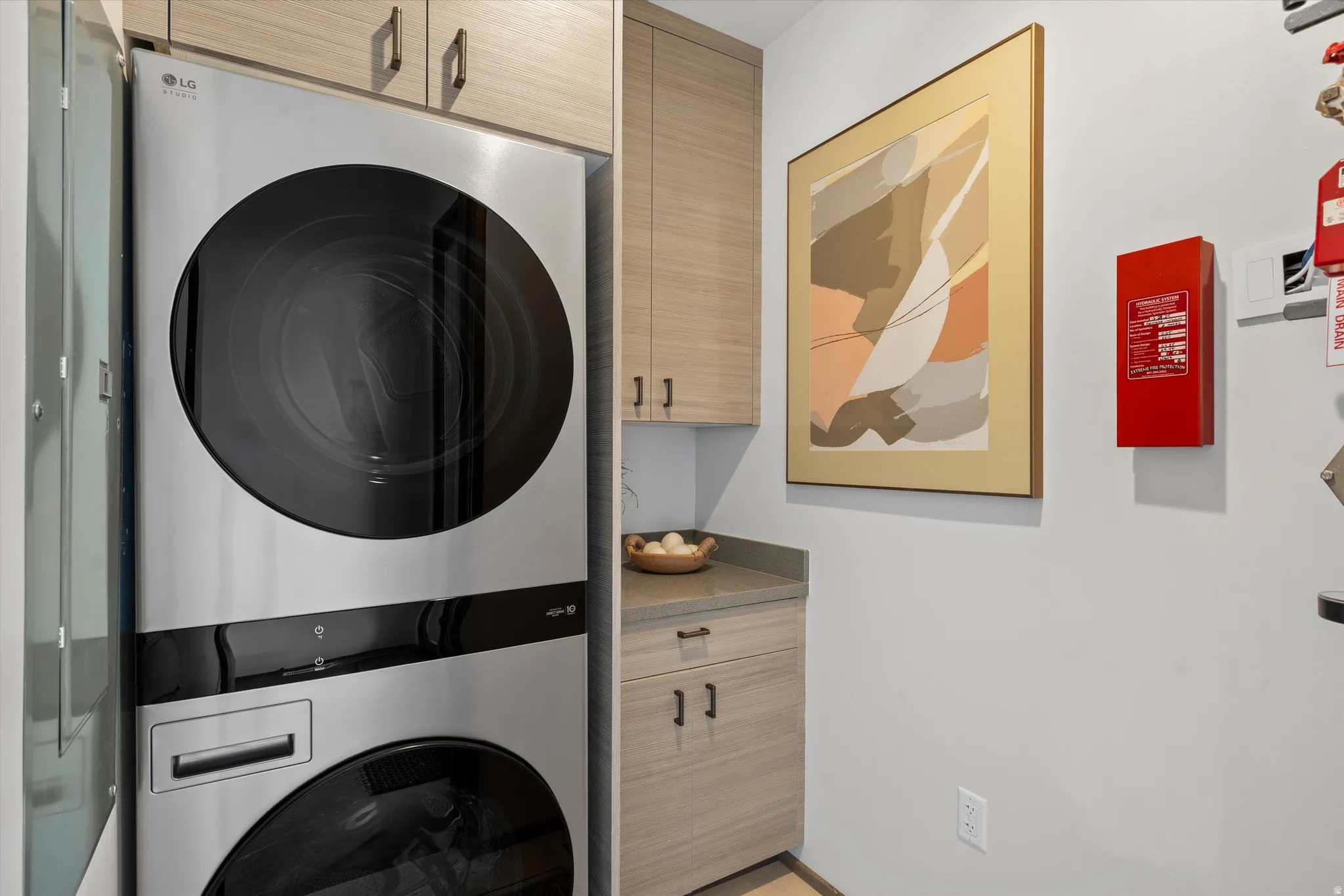 Stacked stainless steel washer and dryer, light wood-finish cabinetry, built-in countertop, and neutral wall color