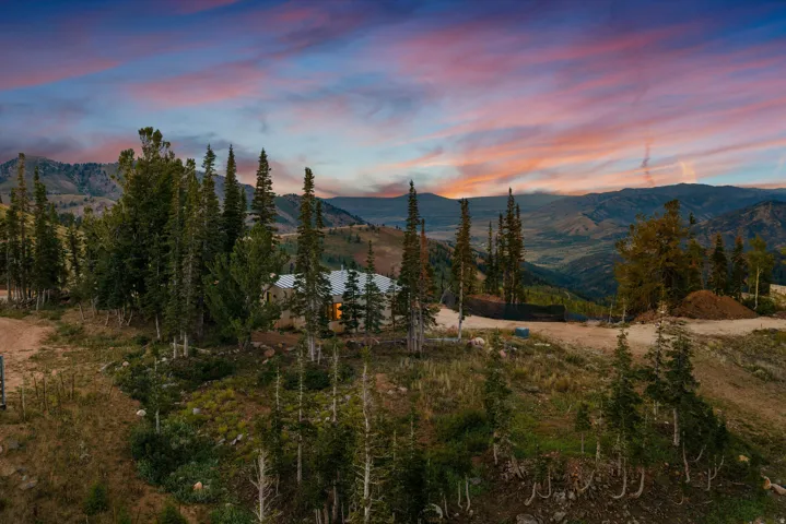 Expansive mountain property featuring mature coniferous and deciduous trees, natural terrain with rolling hillsides, and panoramic sunset vistas across the valley landscape