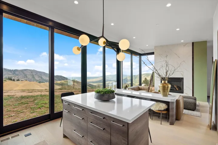 Floor-to-ceiling glass doors, wood-finish flooring, built-in fireplace with a stone surround, recessed lighting, and a modern chandelier