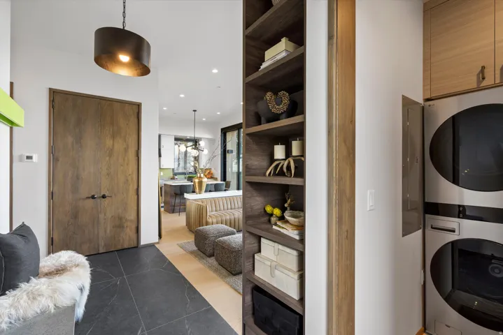 Integrated laundry appliances, built-in shelving, wood-finish double doors, dark tile flooring, and a contemporary pendant light fixture