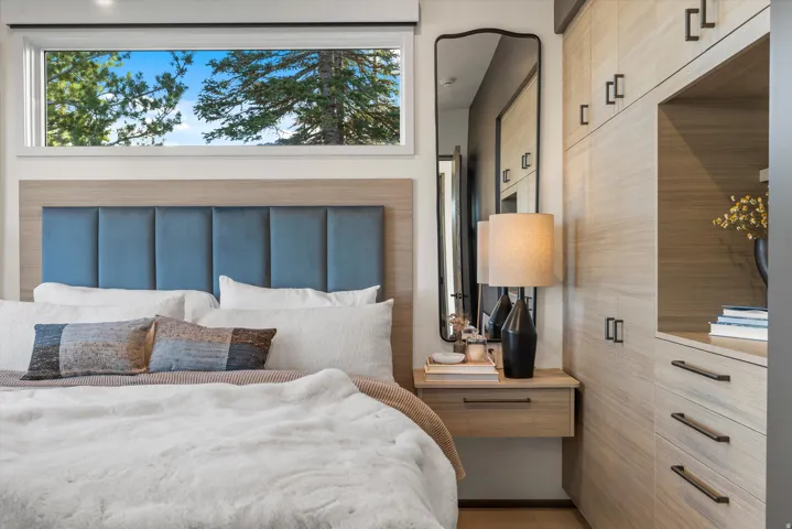 Built-in wood-finish cabinetry, integrated floating nightstand, transom window, full-length mirror with a curved frame, and a panel-tufted headboard
