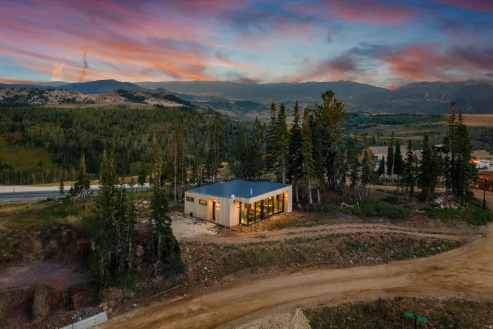 Modern residential structure nestled among mature evergreen trees on expansive grounds, featuring illuminated exterior walls, clean geometric lines, and panoramic mountain and valley vistas across the surrounding landscape