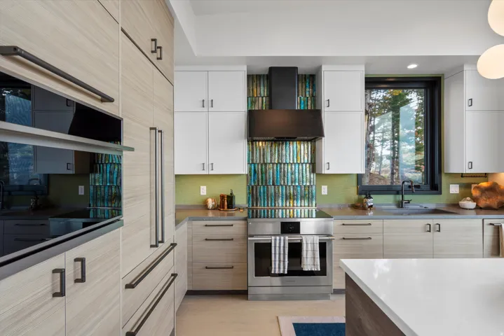 Modern kitchen featuring integrated appliances, light wood-finish cabinetry, a striking multi-tone backsplash, and light countertops