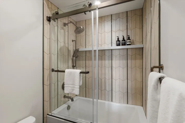 Bathtub with chevron-patterned tile surround, glass shower enclosure, and built-in shower shelf
