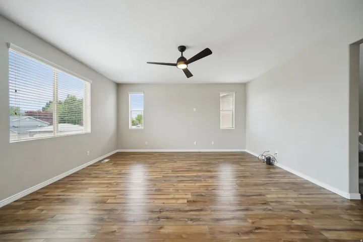Spacious room with wood-finish flooring, multiple windows, and a ceiling fan
