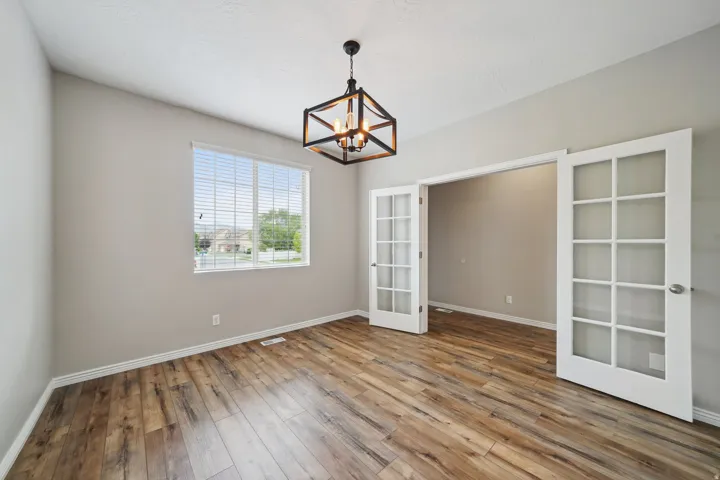 Wood-finish flooring, neutral wall paint, contemporary multi-light chandelier, and French doors with frosted glass panels