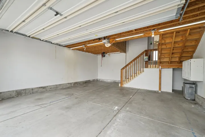 Concrete flooring, exposed wood ceiling beams, built-in staircase with wood railing, white wall-mounted cabinetry, and overhead lighting
