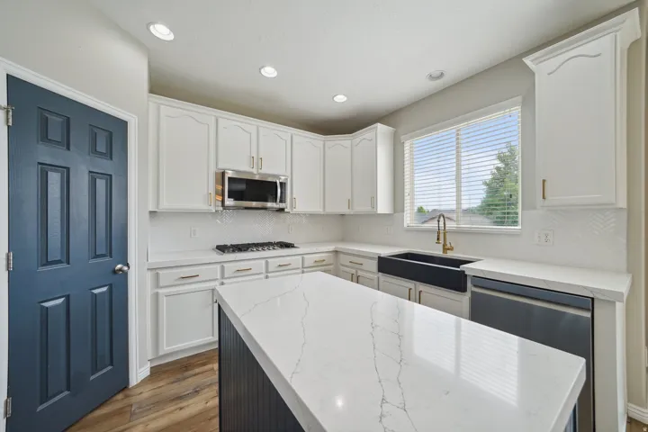 White shaker cabinetry, quartz countertops, wood-finish flooring, a stainless steel gas range, and a farmhouse sink