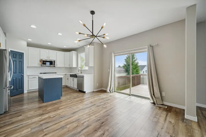 Wood-finish flooring, white cabinetry, dark blue kitchen island, stainless steel appliances, and sliding glass door