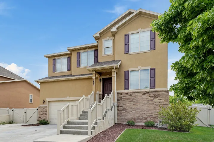 Stucco exterior with brick detailing, covered entry, attached garage, and decorative window shutters