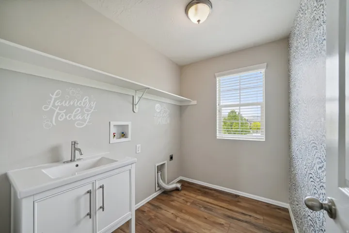 Utility room featuring a white vanity with integrated sink, wood-finish flooring, and a single window with blinds
