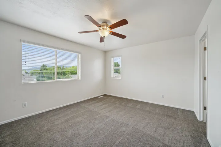 Spacious room featuring carpeting, multiple windows providing natural illumination, and a ceiling fan with integrated lighting