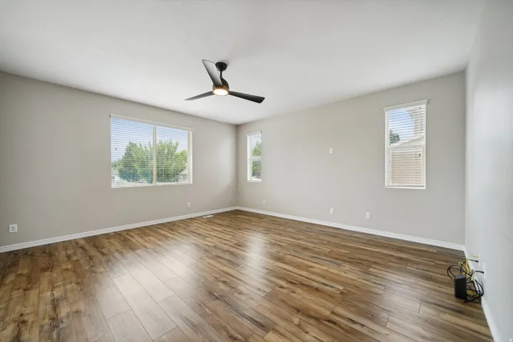 Wood-finish flooring, multiple windows with blinds, modern ceiling fan, and light-toned wall finishes
