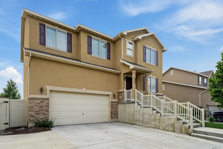 Stucco exterior with brick detailing, multi-pane windows with decorative shutters, integrated two-car garage, covered porch entry, and a concrete driveway