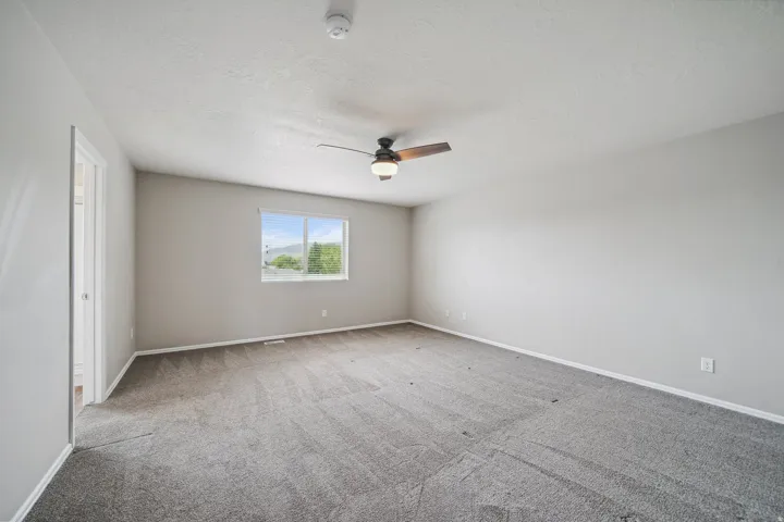 Spacious room featuring carpeting, a ceiling fan with integrated lighting, and a window providing natural illumination