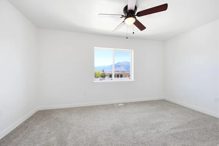 Expansive room featuring light gray carpet flooring and a ceiling fan with integrated lighting