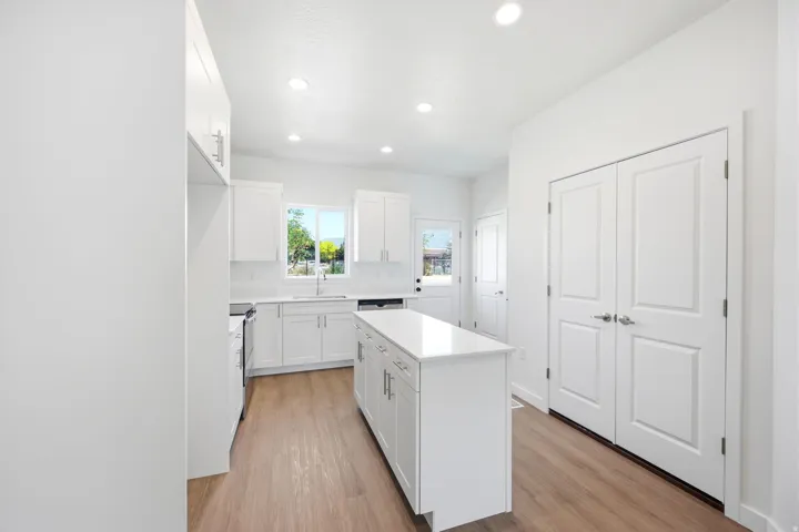 Bright kitchen with white cabinetry, wood-finish flooring, a central island with a solid surface countertop, recessed lighting, and a double-door pantry