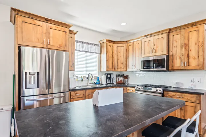 Wood cabinetry, stainless steel appliances, white subway tile backsplash, dark countertops, and recessed lighting
