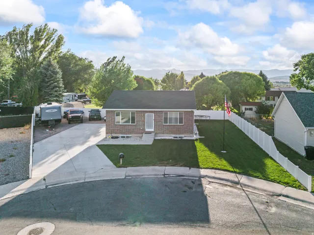 Brick exterior with dark roof shingles, an attached concrete driveway, and a white fence enclosing the property