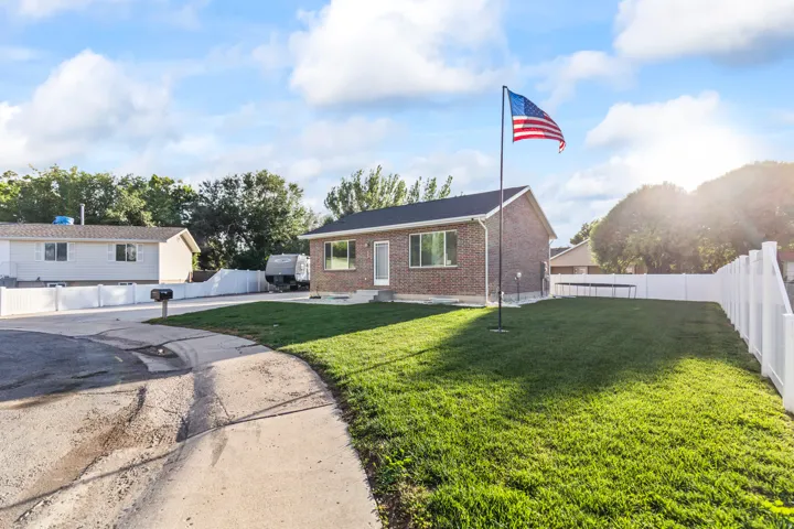 Brick exterior with a dark shingle roof, expansive front lawn, white privacy fencing, and a concrete sidewalk