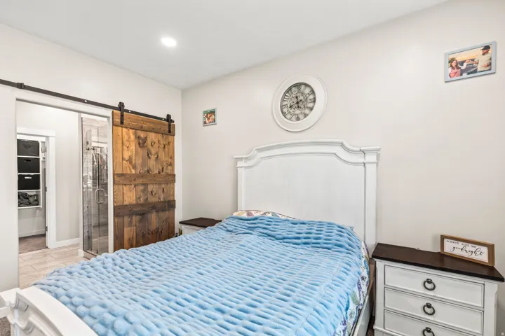 Rustic wood barn door with black hardware, white built-in headboard, recessed lighting, white walls, and built-in white nightstands