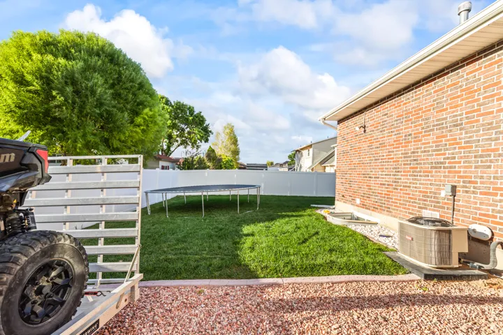 Expansive backyard with a green lawn, white privacy fencing, and a brick exterior wall