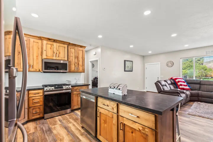 Kitchen featuring wood cabinetry, stainless steel appliances, dark countertops, white subway tile backsplash, and wood-finish flooring