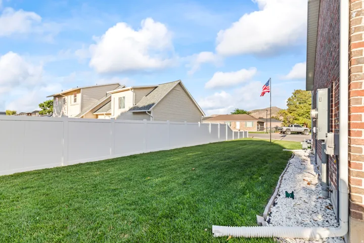 Expansive side yard featuring a manicured lawn, full privacy fencing, brick exterior, and a white rock bed