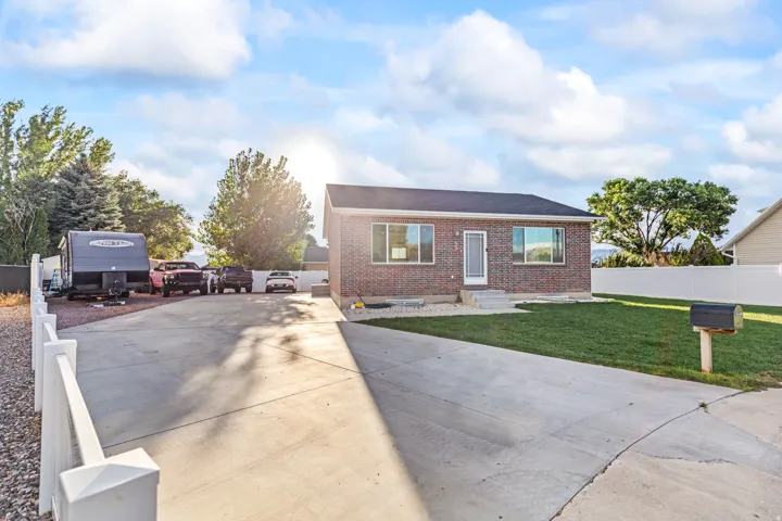 Brick facade with dark roof, concrete driveway, white fencing, and a manicured lawn