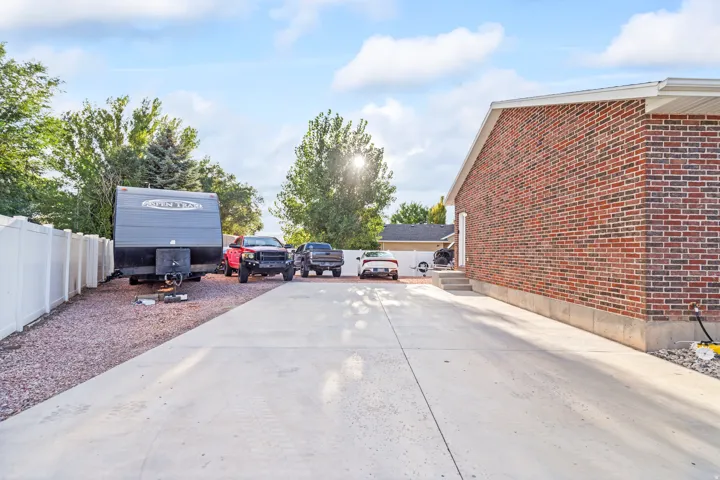 Expansive concrete driveway with brick-finish exterior, white vinyl fencing, and gravel parking area