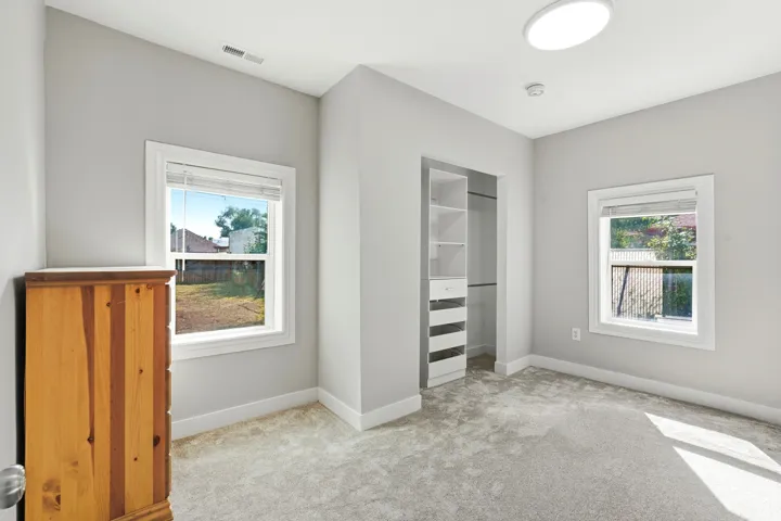 Carpeted flooring, two windows, built-in closet organization system, and a flush-mount ceiling light fixture