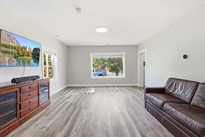 Spacious recreation room featuring plank-style wood-finish flooring, recessed ceiling lighting, and large windows framed by white trim that flood the space with natural light