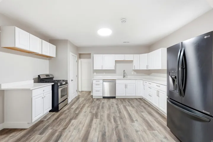 Kitchen featuring wood-finish flooring, white cabinetry, a stainless steel dishwasher, a stainless steel range, and a black refrigerator