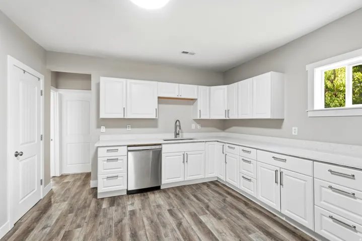 Spacious kitchen featuring white cabinetry, light-toned countertops, a stainless steel dishwasher, and wood-finish flooring