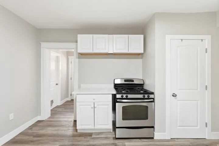 White cabinetry, stainless steel range, light-toned countertops, and wood-finish flooring
