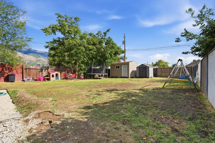 Expansive backyard featuring mature trees, two storage sheds, and mountain backdrop