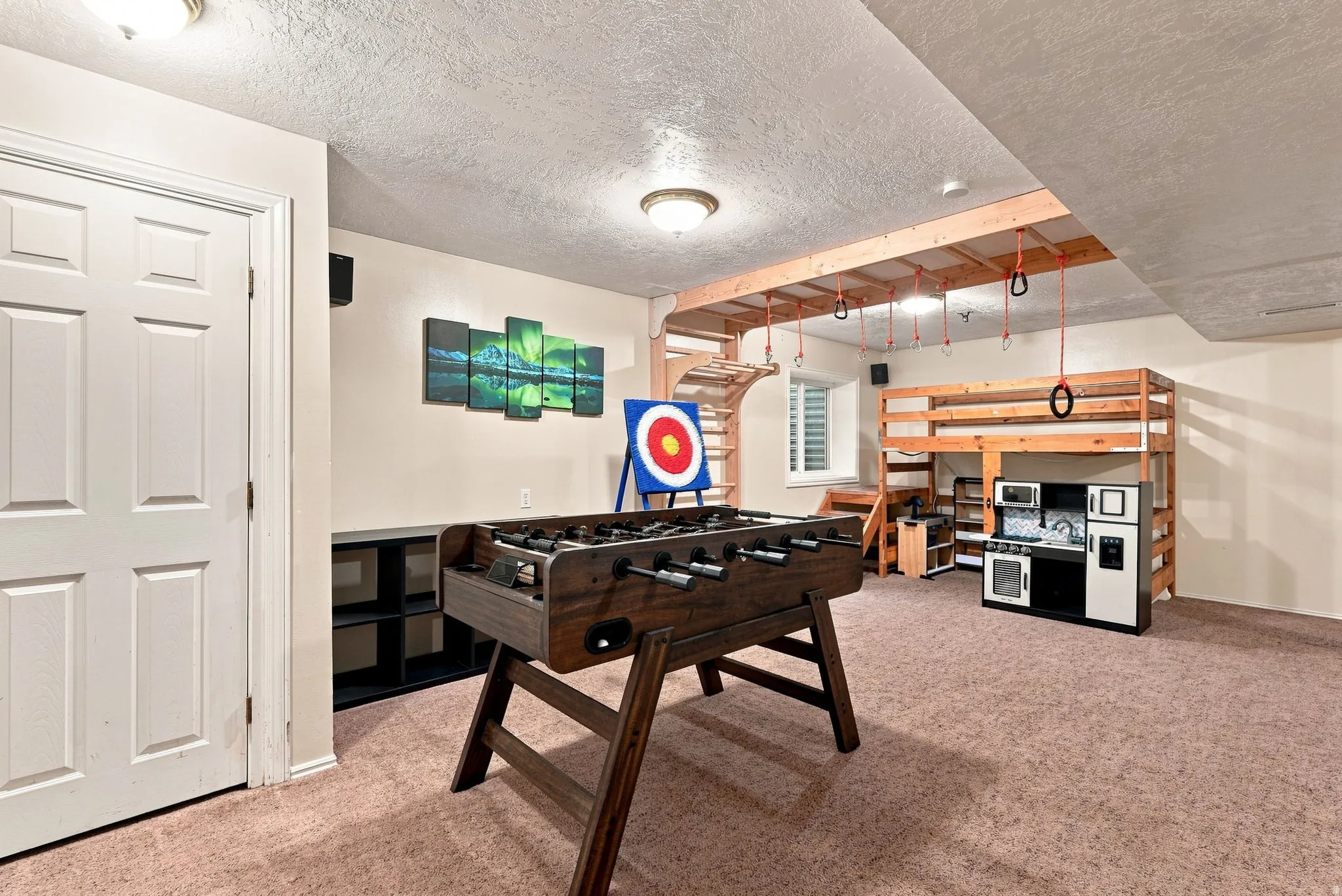 Carpeted room with a built-in wooden structure featuring a climbing wall, suspended rings, and a raised platform