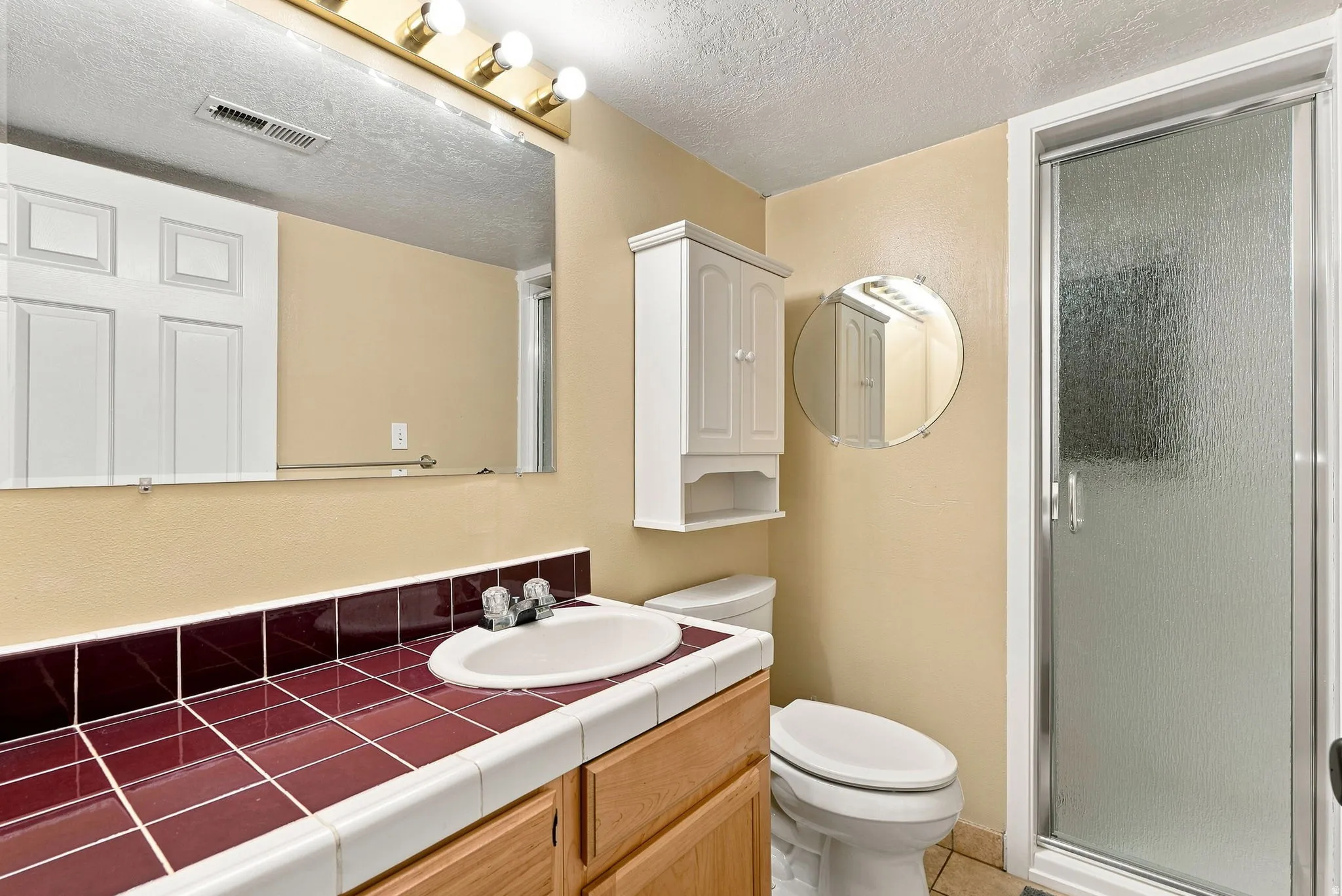 Bathroom featuring a vanity with a white basin, red tile countertop, and wood-finish cabinetry