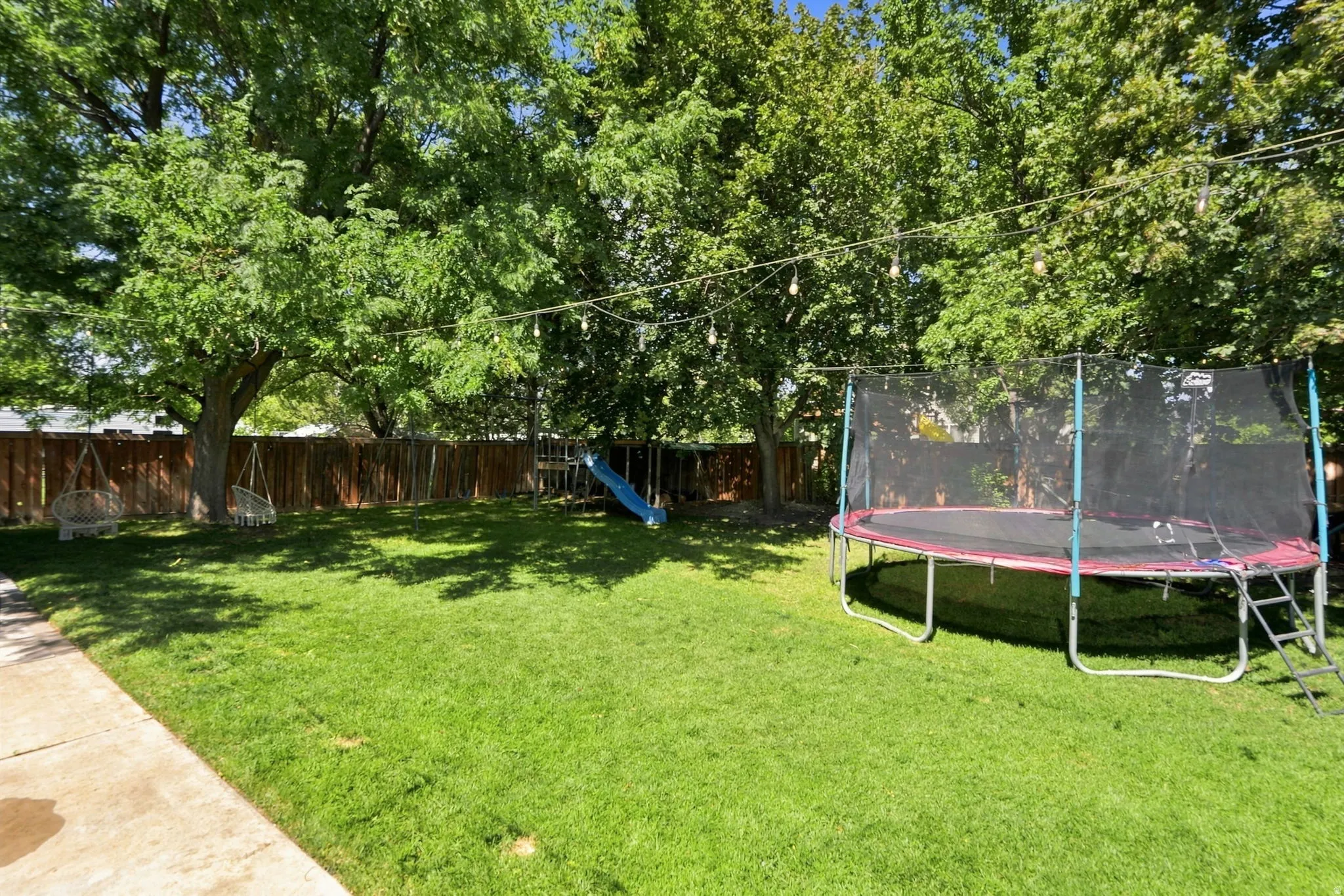 Expansive backyard featuring a green lawn, mature trees, and a wood privacy fence