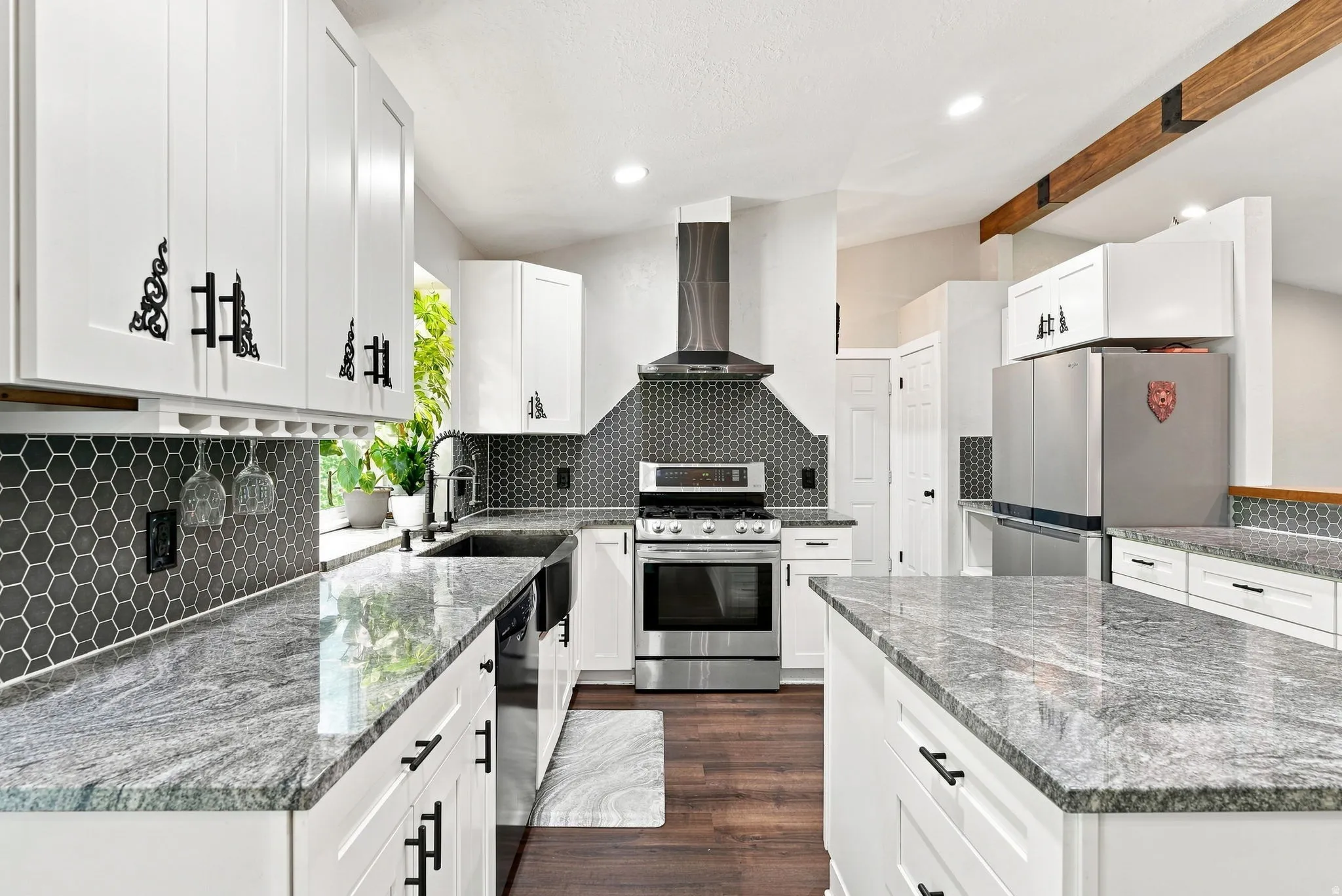 White cabinetry with dark ornamental hardware, a hexagonal tile backsplash, light-toned countertops, stainless steel appliances, and wood-finish flooring