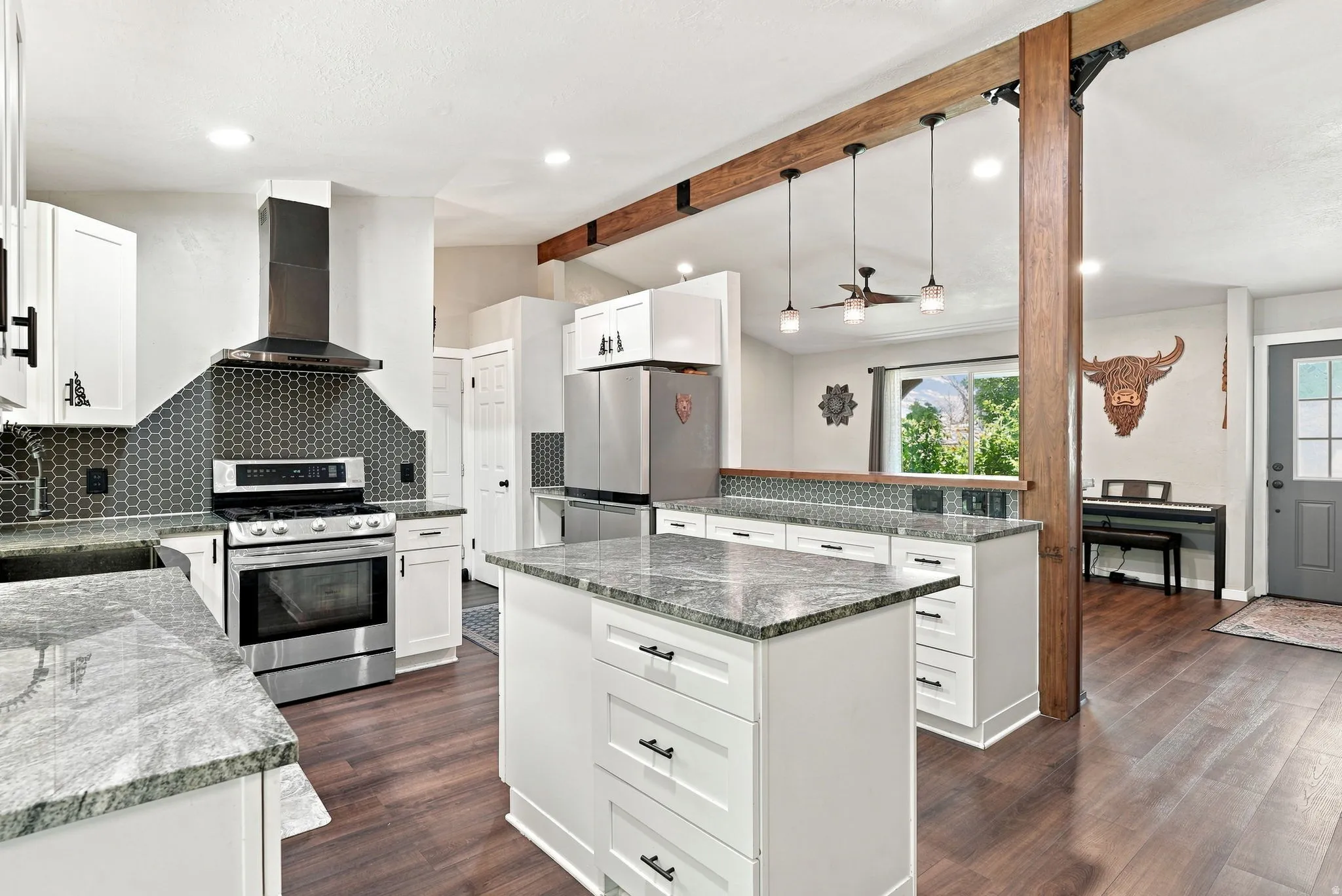 Kitchen featuring white cabinetry, stainless steel appliances, hex tile backsplash, wood-finish flooring, and a central island with a granite countertop