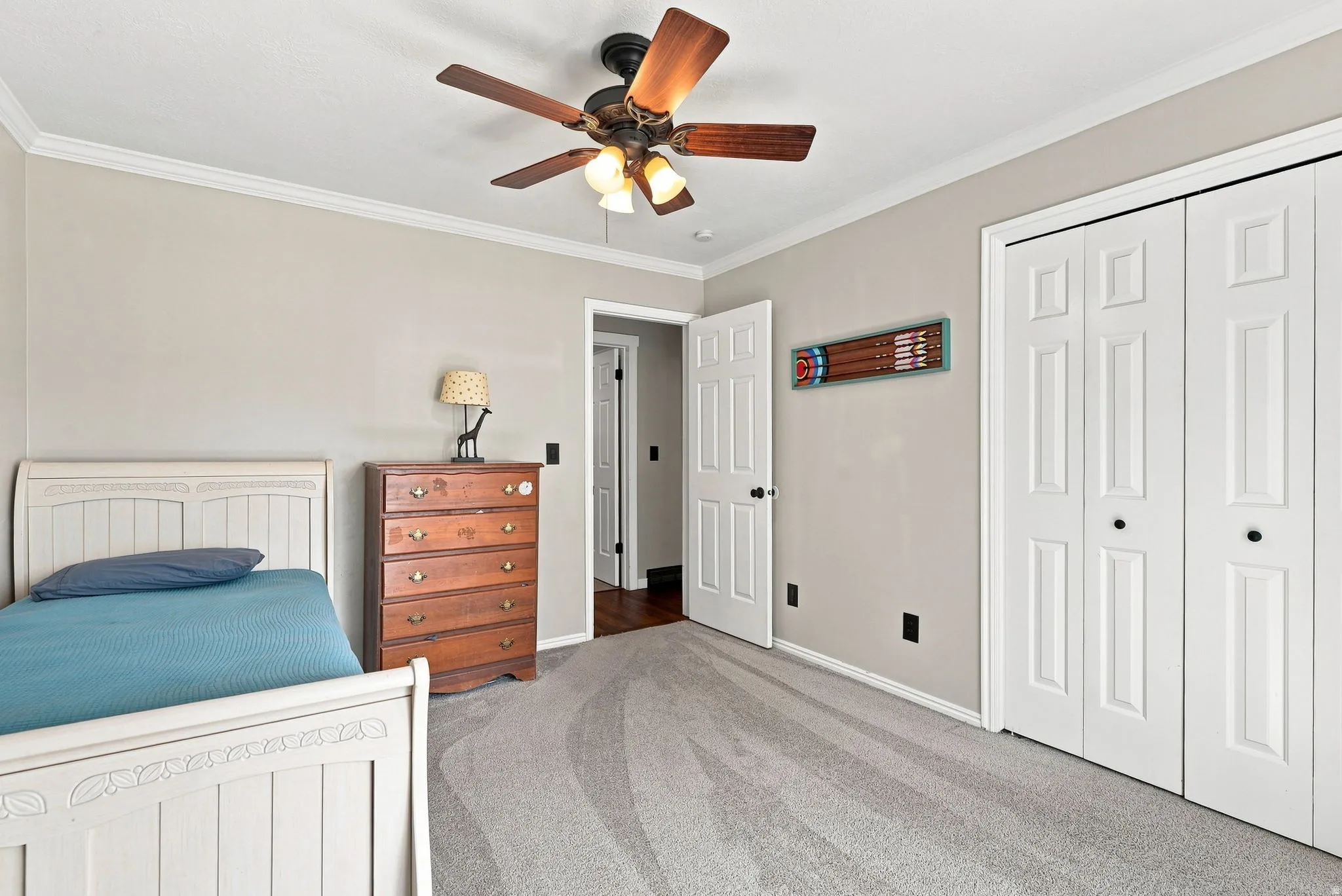 Crown molding, textured carpeting, double bifold closet doors, ceiling fan with integrated lighting, and a paneled interior door