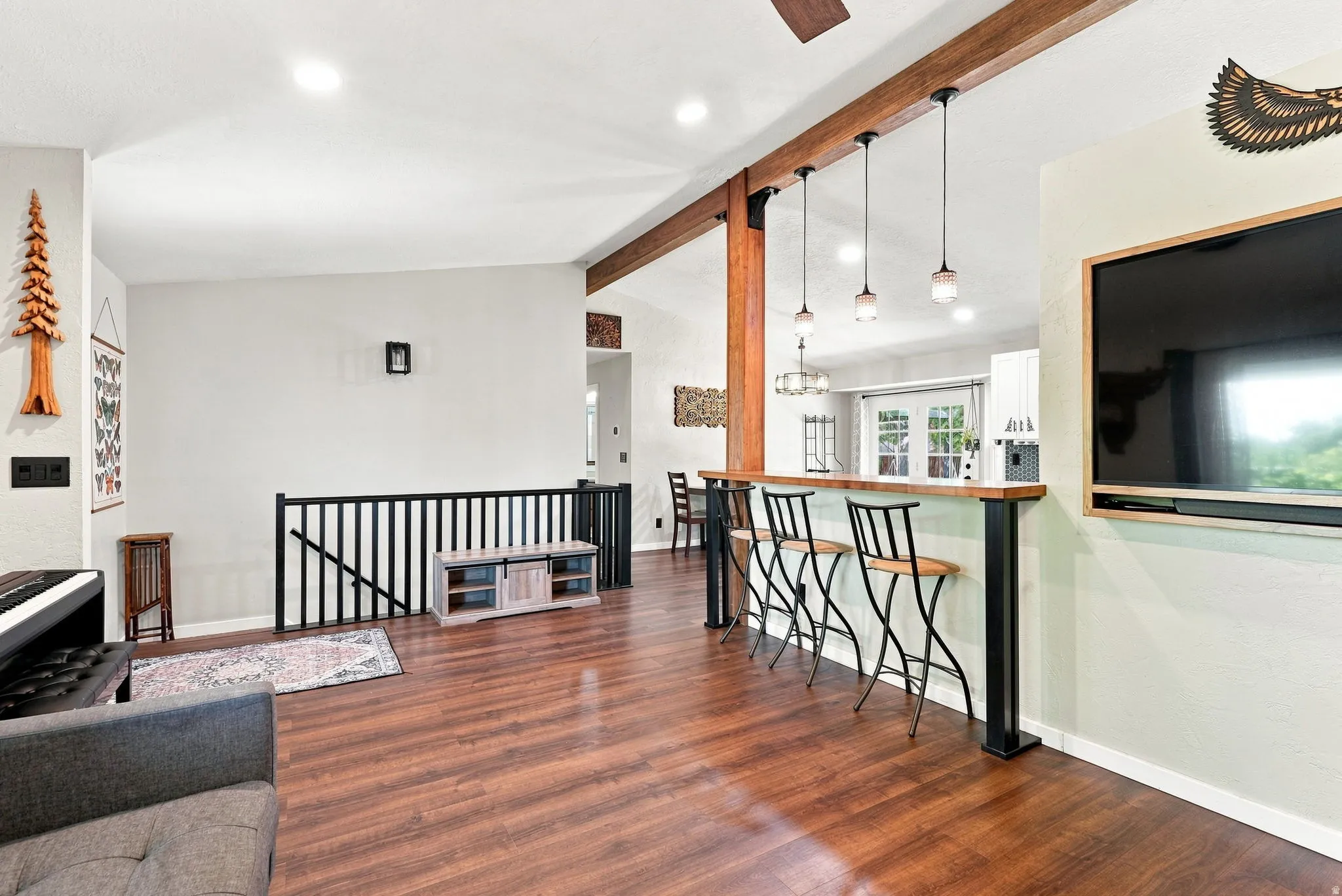 Wood-finish flooring, exposed wood beams, pendant lighting, and a built-in breakfast bar create a cohesive design