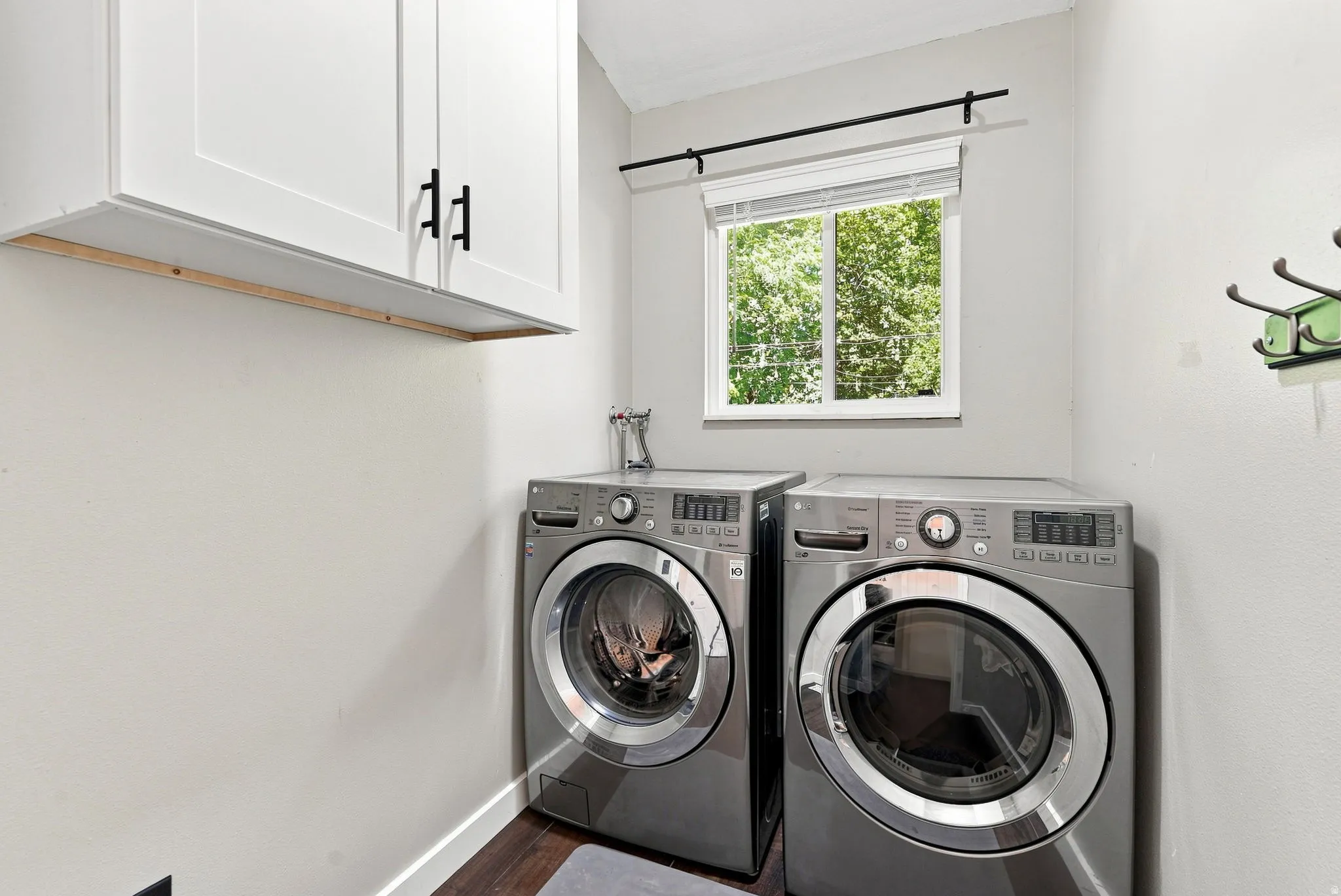 White shaker-style cabinetry with matte black hardware, a window with natural light, and wood-finish flooring