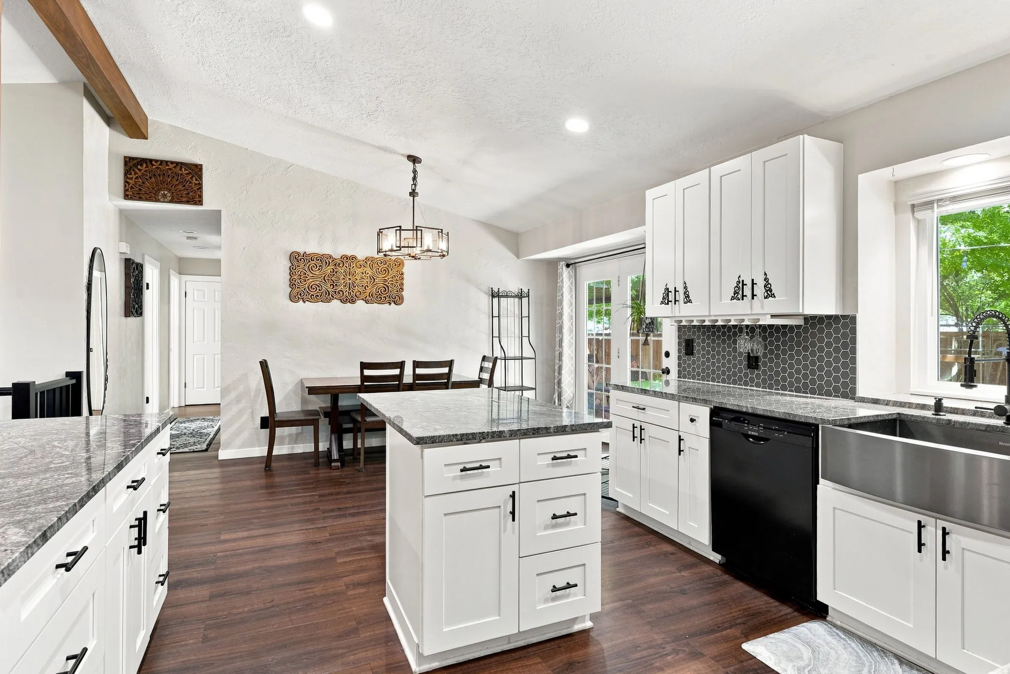 Vaulted ceiling, wood-finish flooring, white cabinetry, dark gray countertops, and a stainless steel farmhouse sink