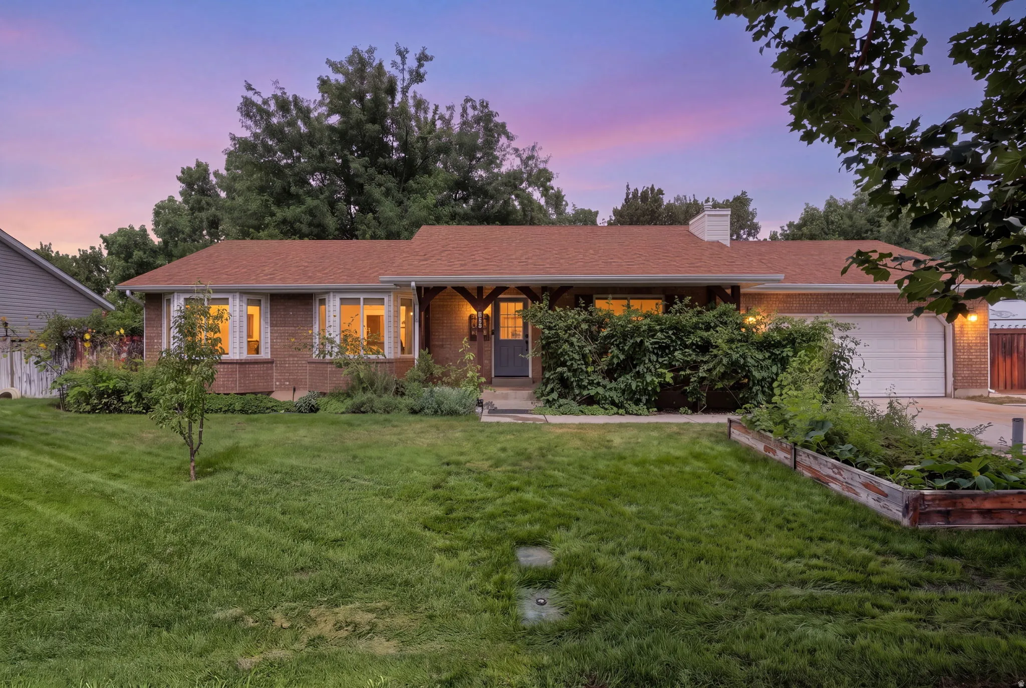 Brick exterior with a brown shingle roof, attached garage, and a front lawn with established landscaping